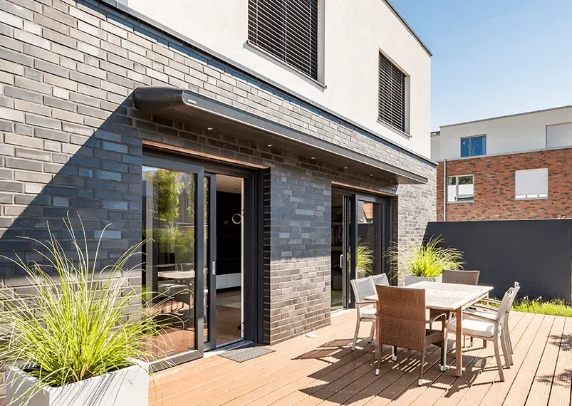 Eine Terrasse mit Tisch und Stühlen vor einem Backsteingebäude.