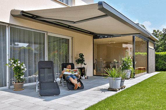 Eine Person sitzt auf einer Terrasse unter einer Markise.