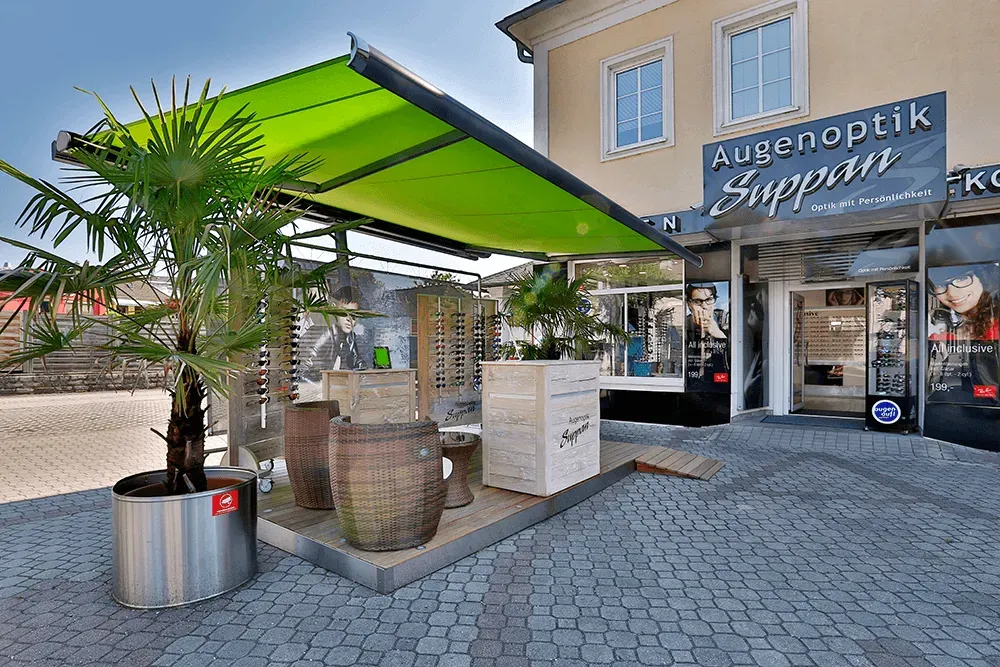 Eine Ladenfront mit einer grünen Markise und Topfpflanzen davor.