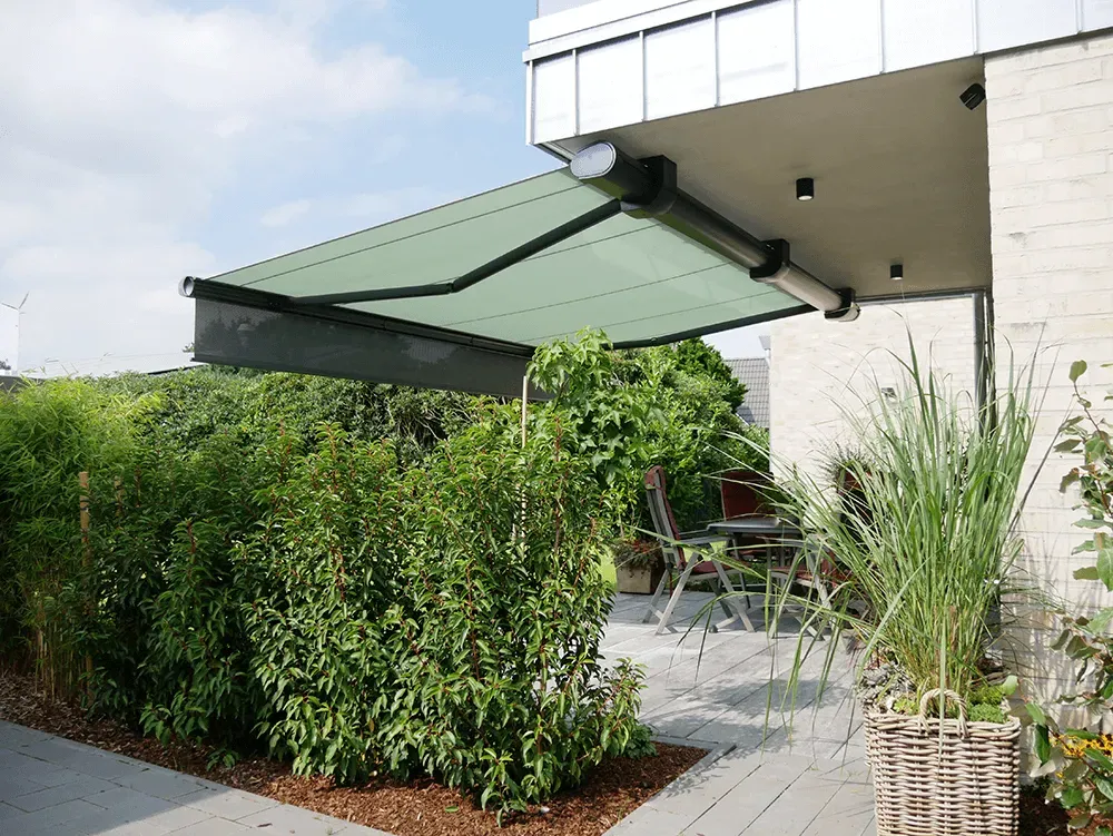 Eine grüne Markise überdacht eine Terrasse mit Stühlen und einem Tisch