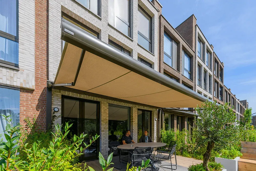 Ein Mann sitzt an einem Tisch unter einem Vordach an der Seite eines Gebäudes.