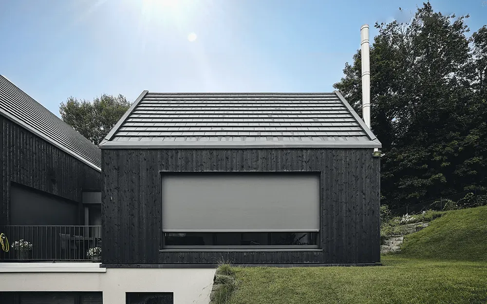 Ein schwarzes Haus mit einem grauen Dach und einem großen Fenster.