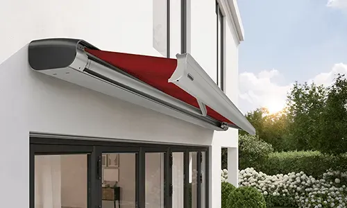 Ein weißes Haus mit einer roten Markise an der Seite.