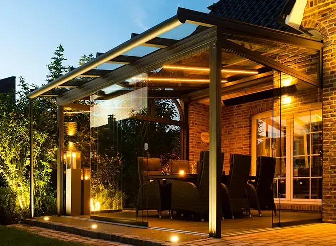 Eine überdachte Terrasse mit Tisch und Stühlen ist nachts beleuchtet.