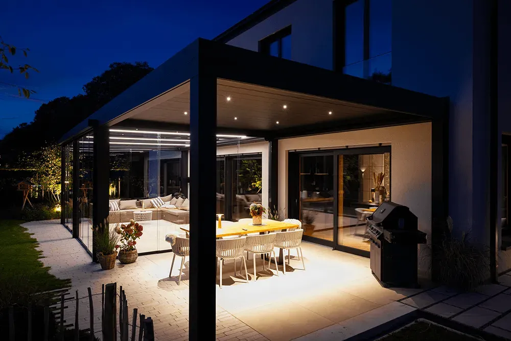 Eine Terrasse mit Tisch und Stühlen unter einer Pergola bei Nacht.