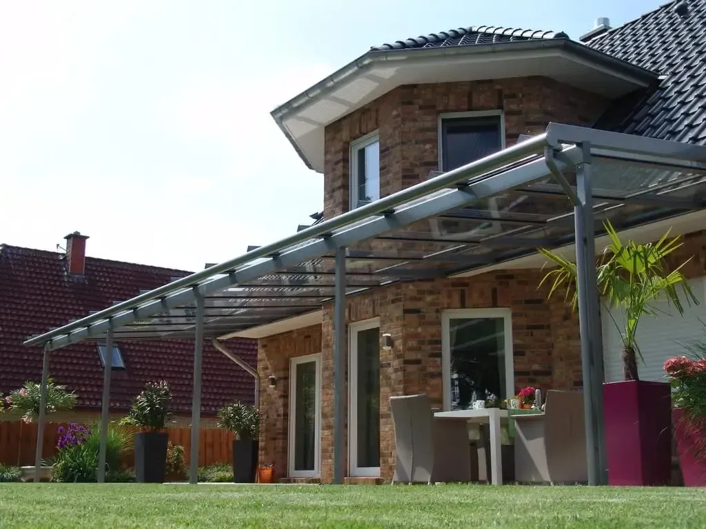 Ein Backsteinhaus mit einer Glaspergola und einem Tisch und Stühlen davor.