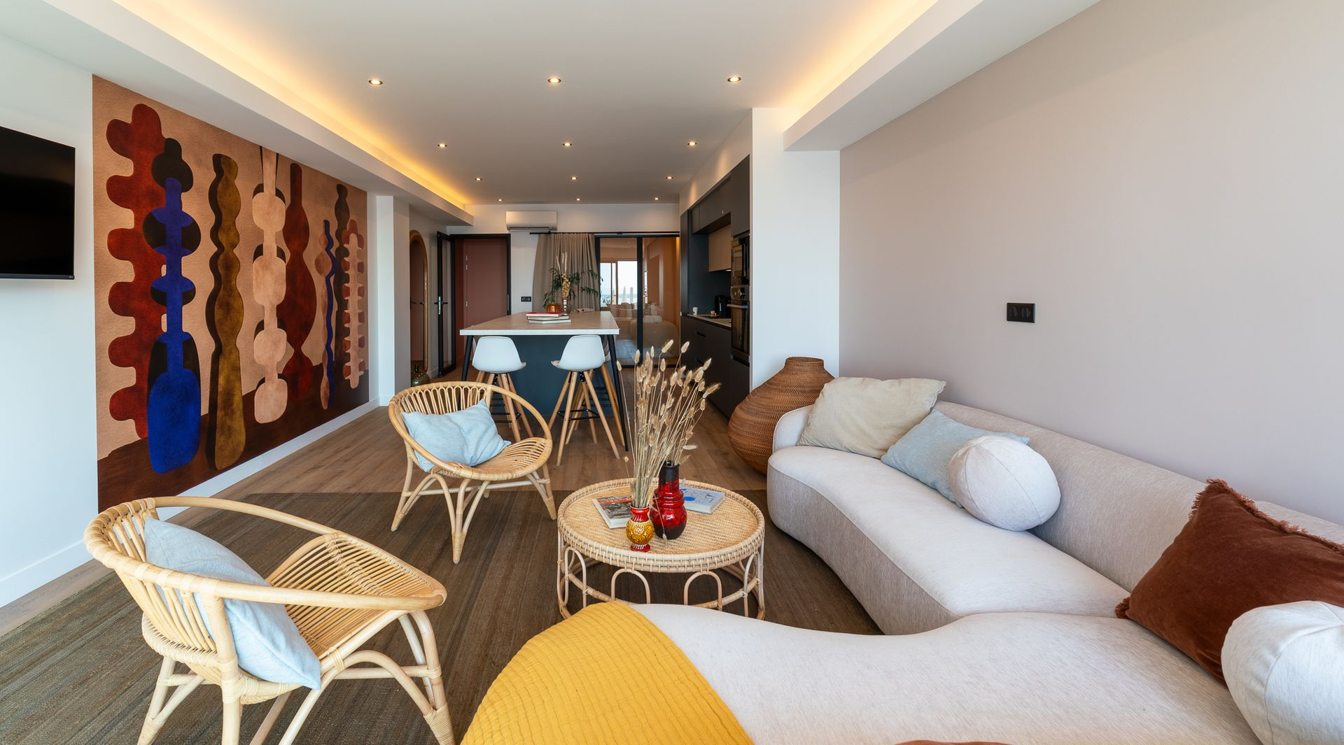 Salon moderne avec canapé blanc, fauteuils en osier, tableaux colorés et grandes fenêtres donnant sur la mer