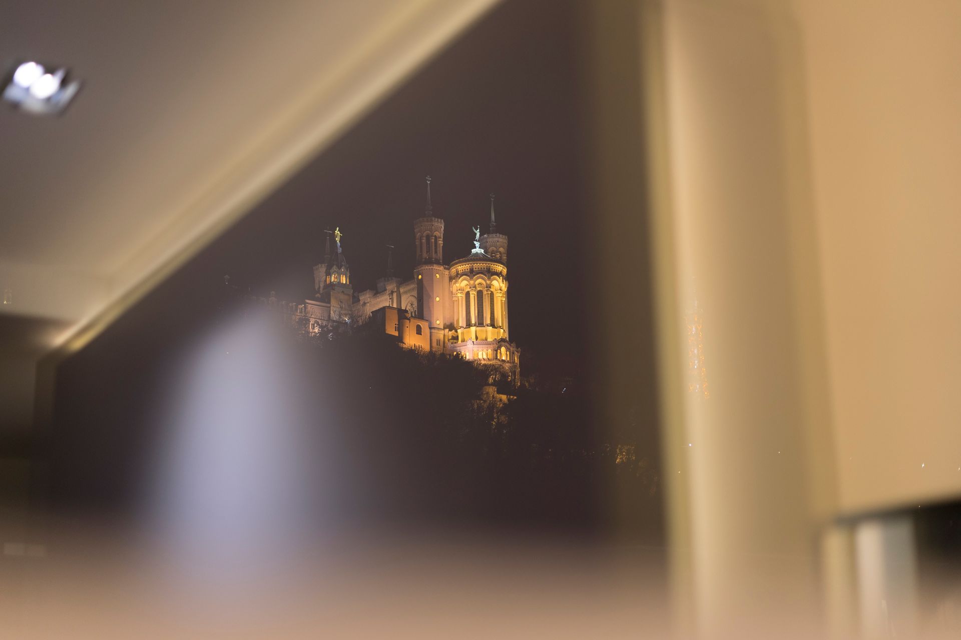 Basilique Fourvière la nuit, illuminée, vue à travers une fenêtre de la Suite Nuances MiHotel à Lyon.
