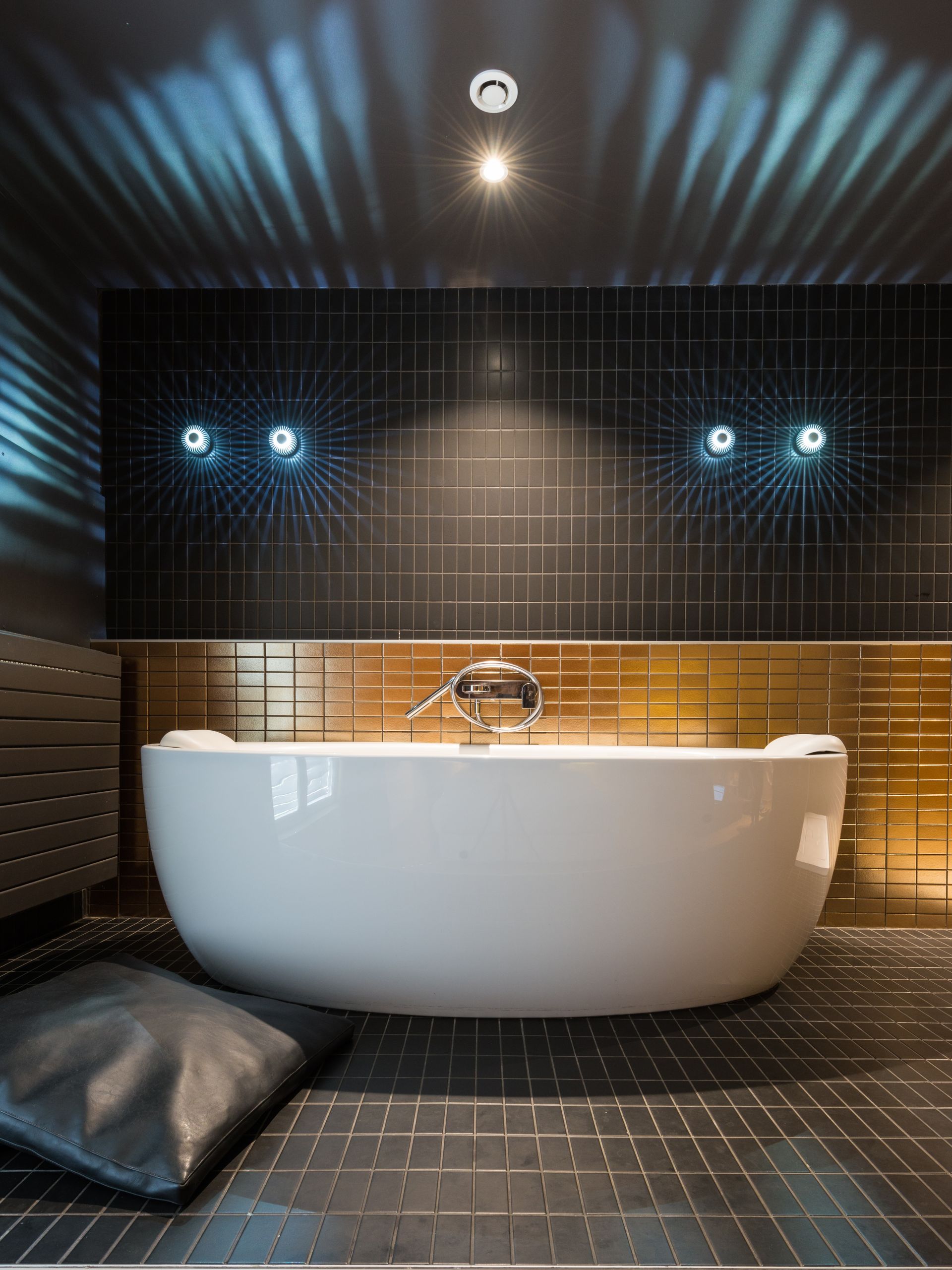 Salle de bains luxueuse avec baignoire îlot, chaise longue rouge et œuvres d'art sur les murs roses.