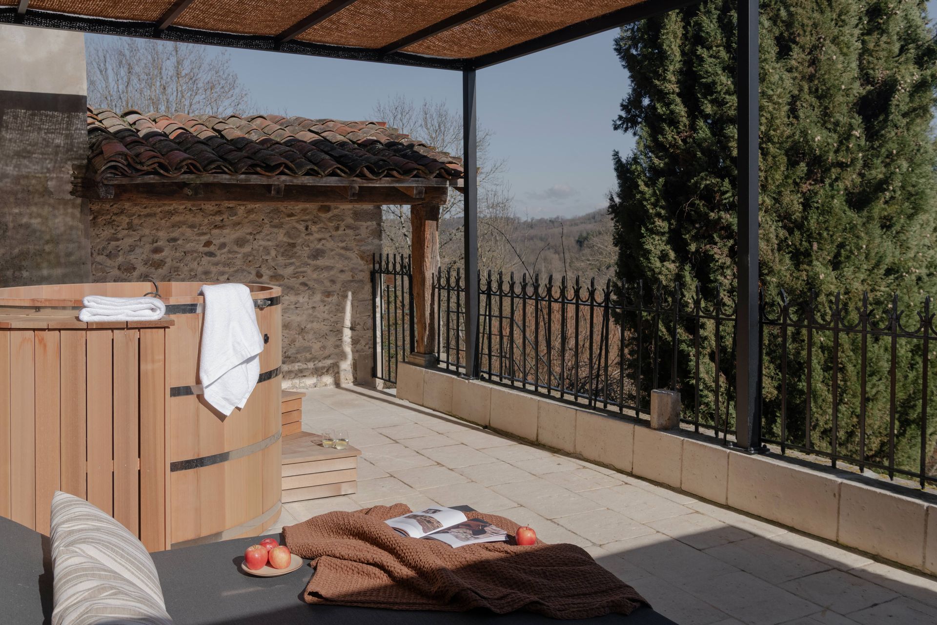 Bain à remous en bois sur une terrasse avec chaise longue, couverture et vue imprenable sur les montagnes.