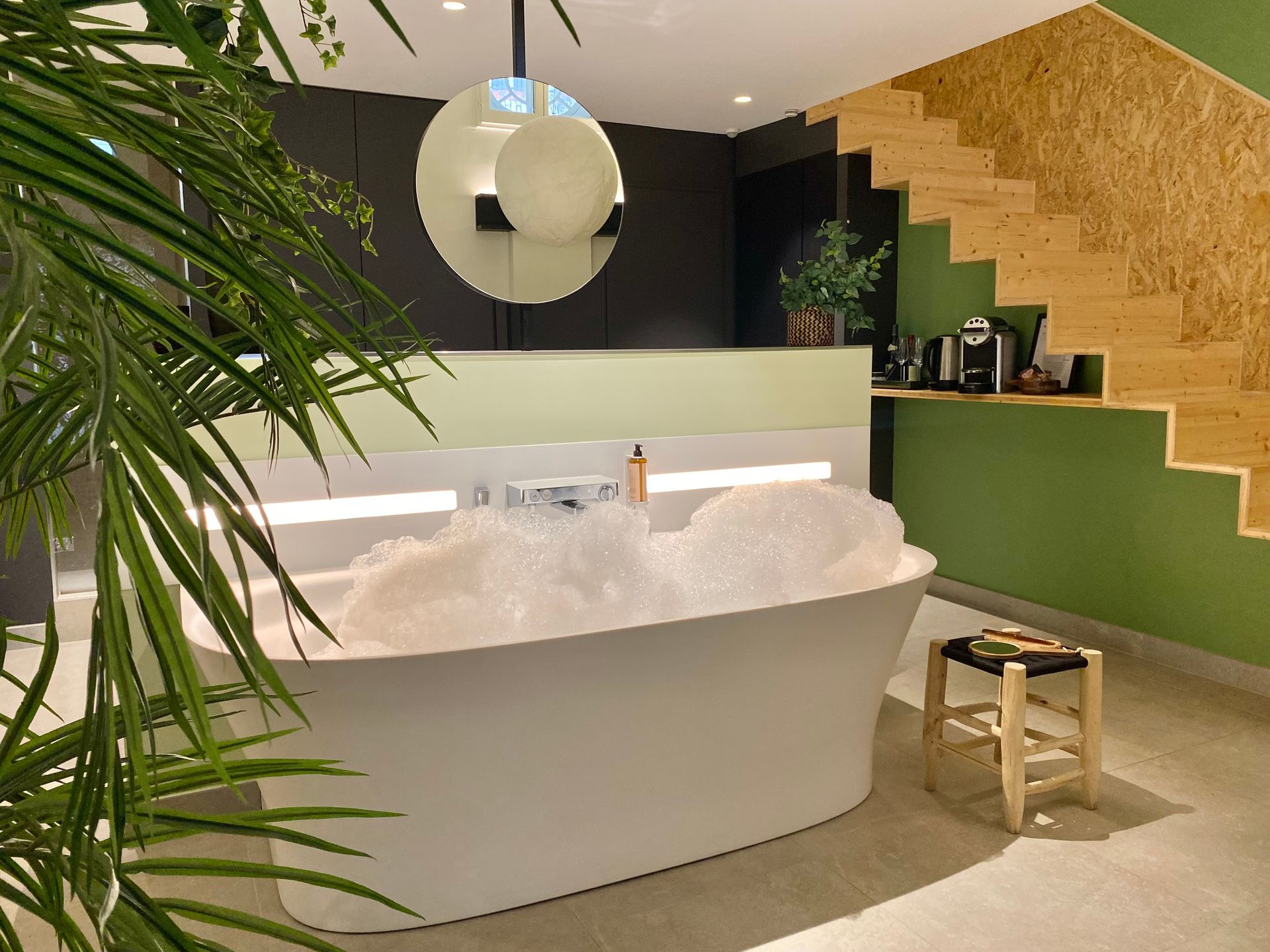 Salle de bain spa moderne avec baignoire îlot, bulles, murs verts et mur d'accent d'escalier