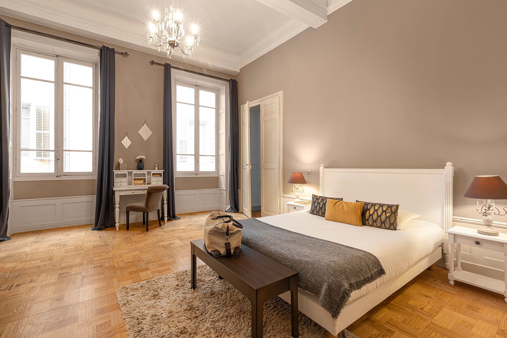 Chambre avec poutres apparentes, tapisserie, lit, miroir rond et mur en pierre.