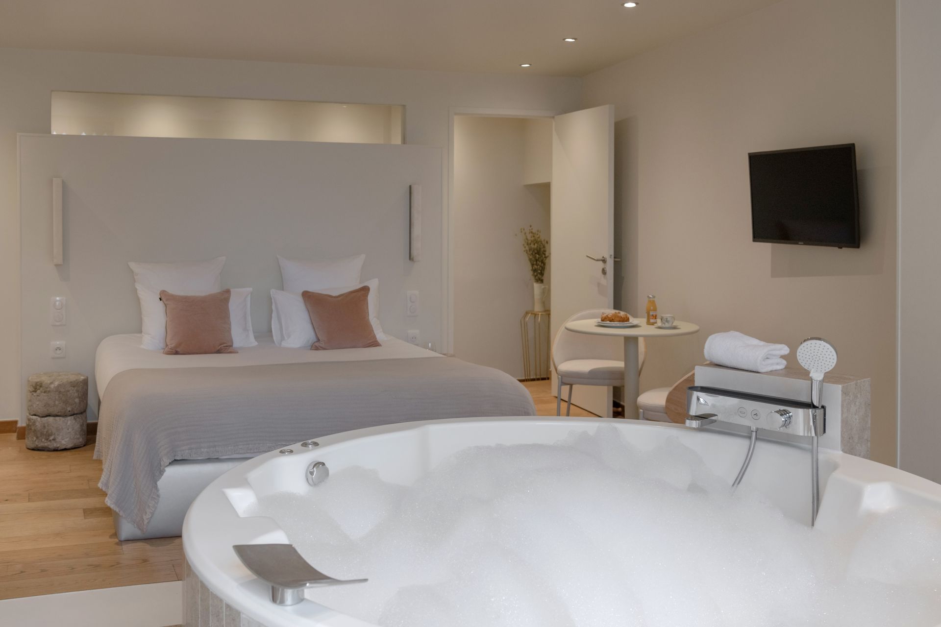 Salle de bains moderne avec baignoire, miroir rond et deux douches ; carrelage beige.