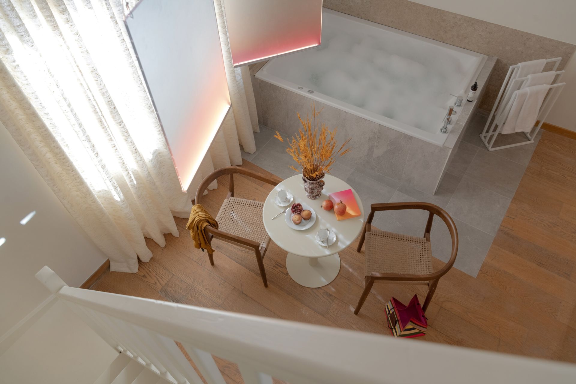 Chambre d'hôtel avec salle de bain ouverte, murs gris, lit, chaises et cheminée.