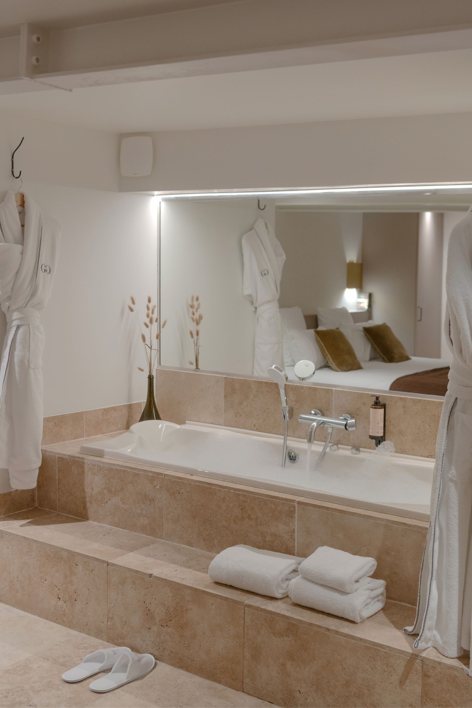 Salle de bains luxueuse avec baignoire îlot, chaise longue rouge et œuvres d'art sur les murs roses.