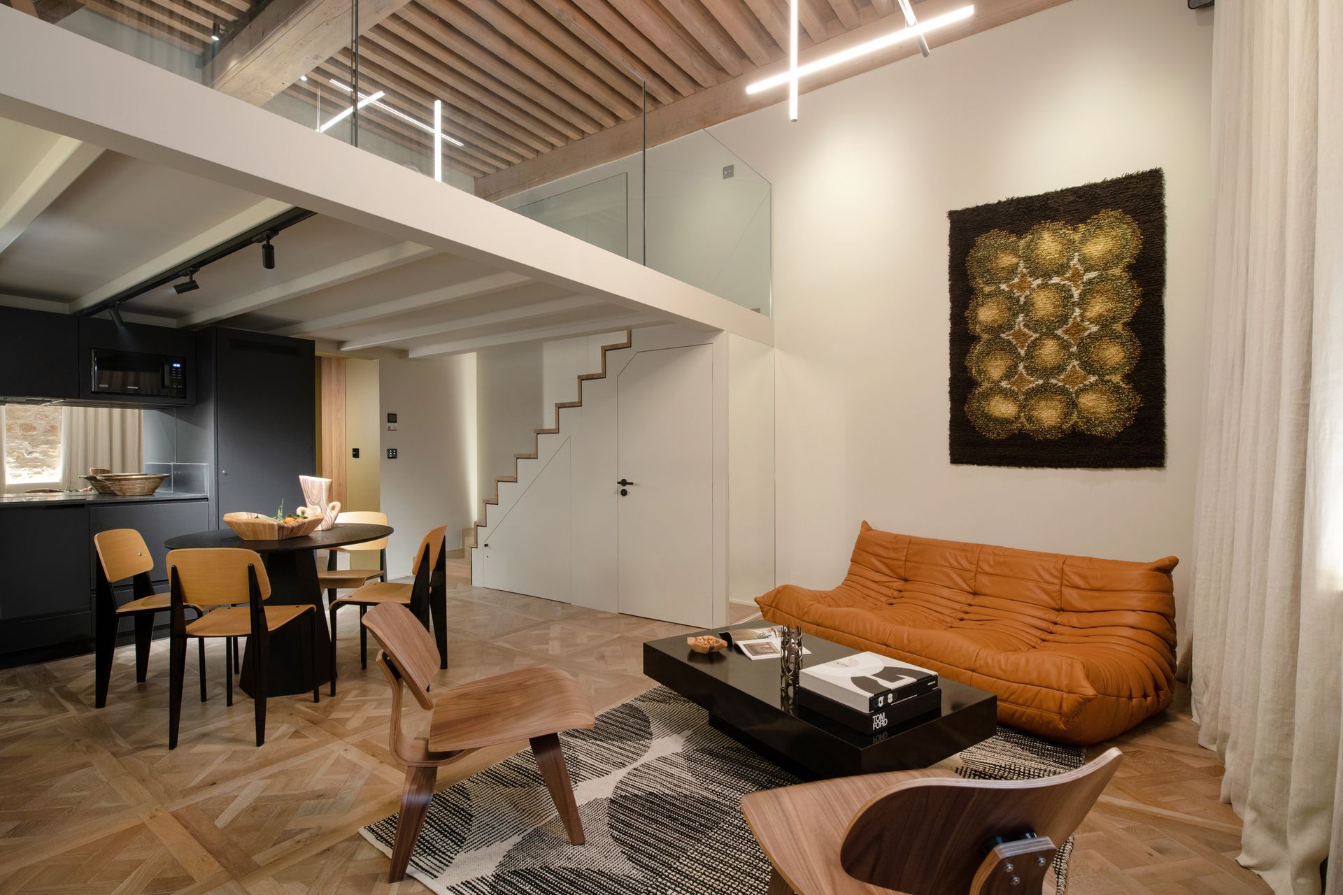 Salon d'appartement moderne avec mezzanine, canapé ligne roset togo, table basse noire, œuvres d'art et coin repas.