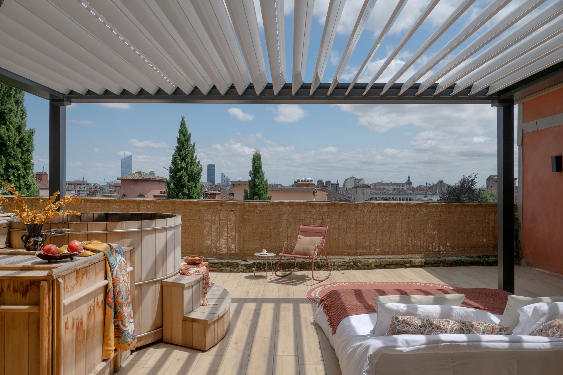 Terrasse sur le toit avec jacuzzi, chaise longue, vue sur la ville et pergola ombragée.
