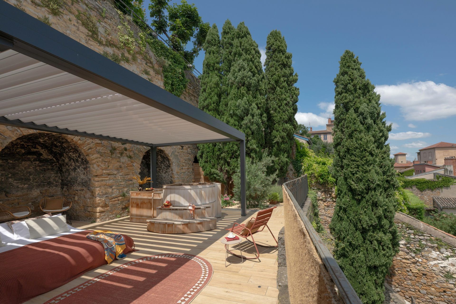 Terrasse ensoleillée avec chaises longues, pergola, muret en pierre et grands cyprès offrant une vue imprenable.