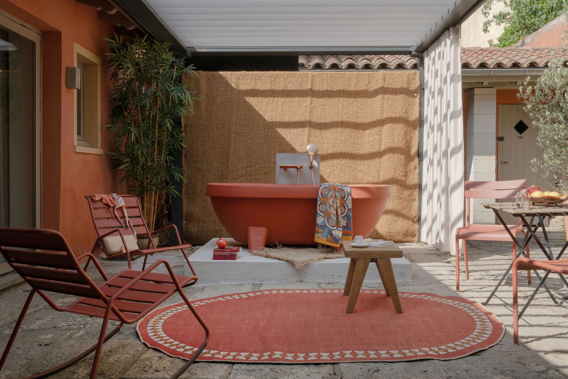 Terrasse couverte avec chaises rouges, tapis rond, petite table et barbecue intégré.