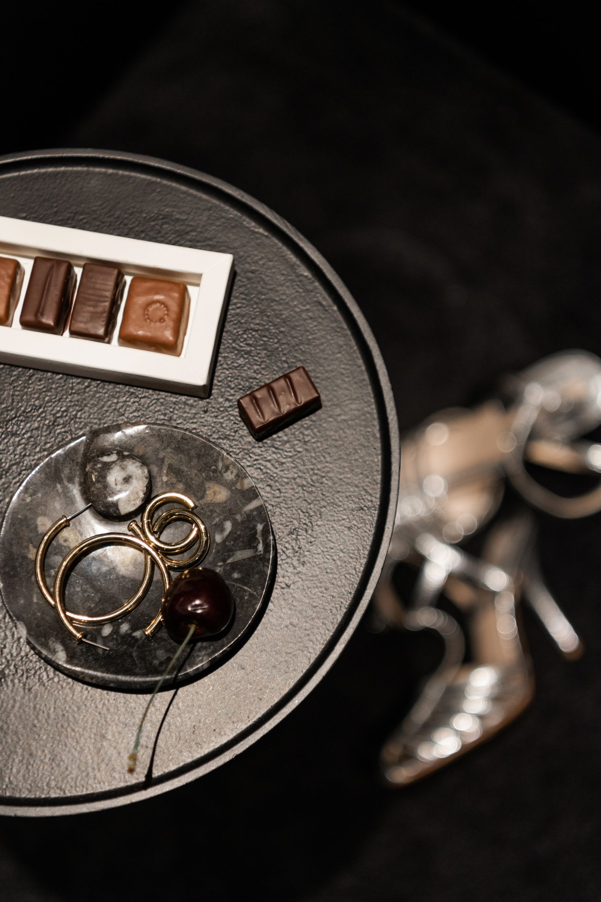 Des bijoux et de petits objets bruns sur un plateau rond et sombre, avec des breloques en métal à côté.