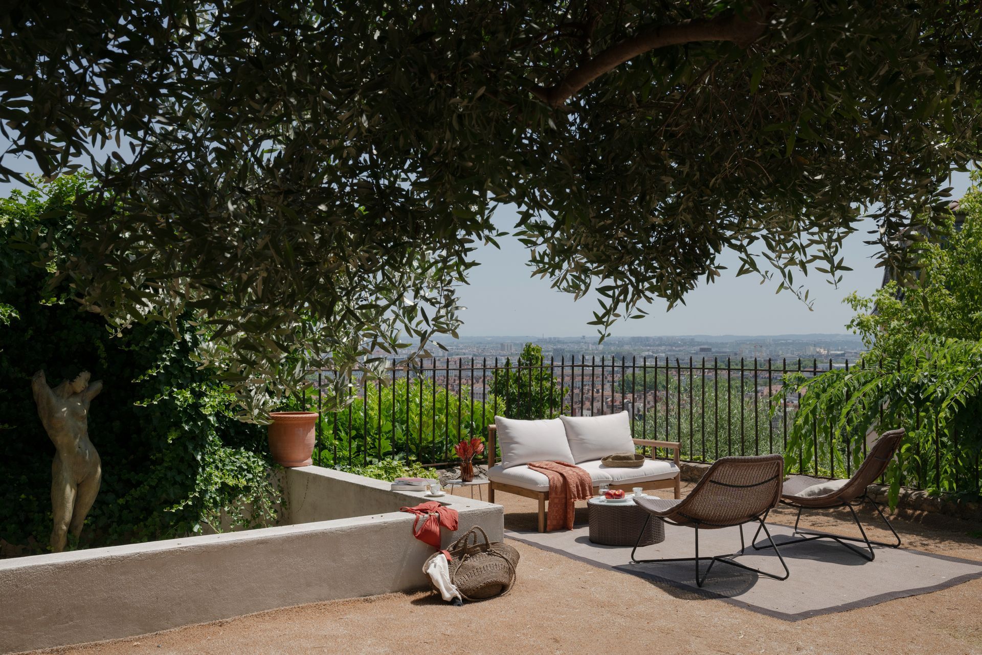 Terrasse extérieure avec sièges, à l'ombre des arbres, avec vue sur la ville.