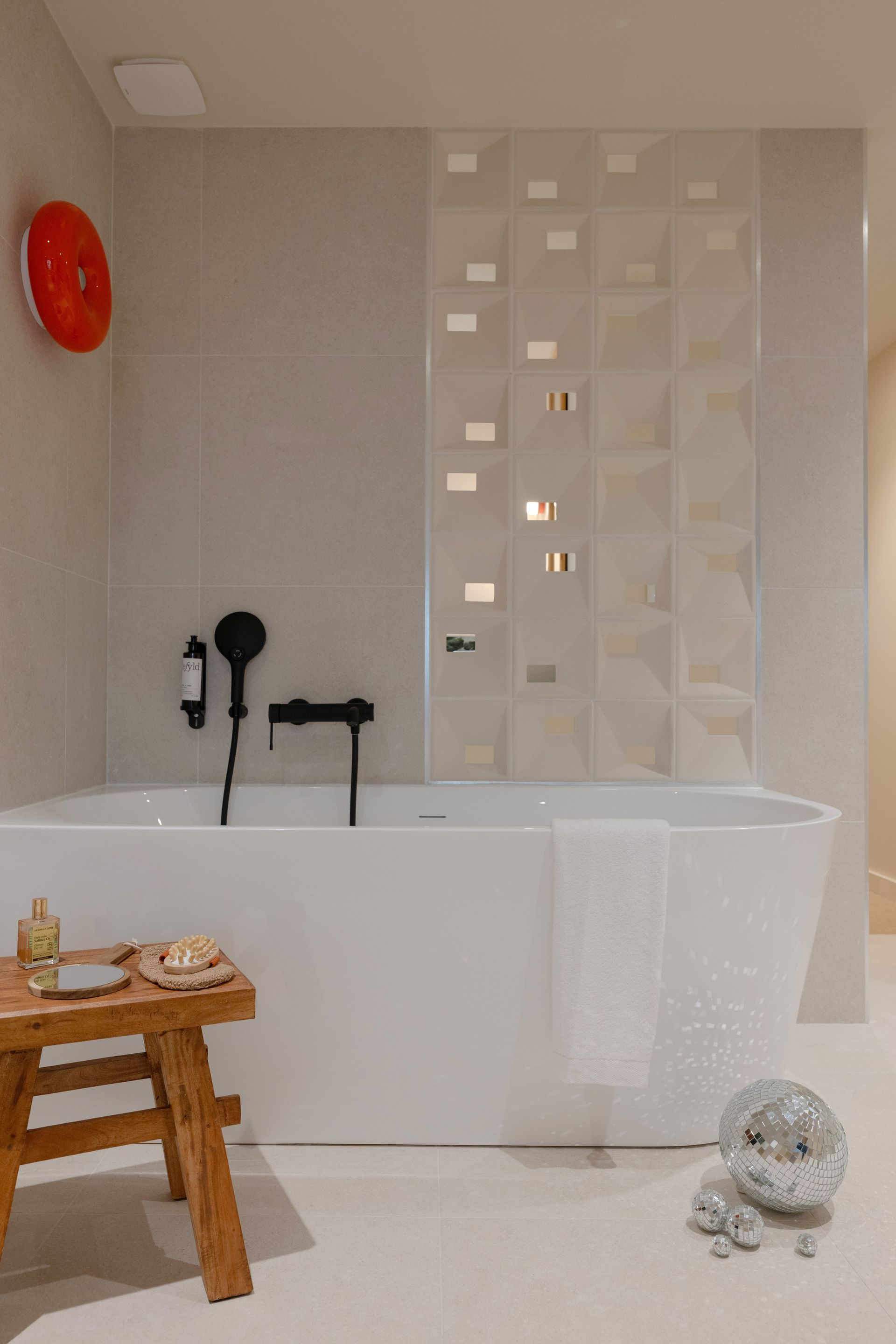 Salle de bains moderne avec baignoire îlot, rideau de douche blanc, tabouret en bois et horloge murale rouge