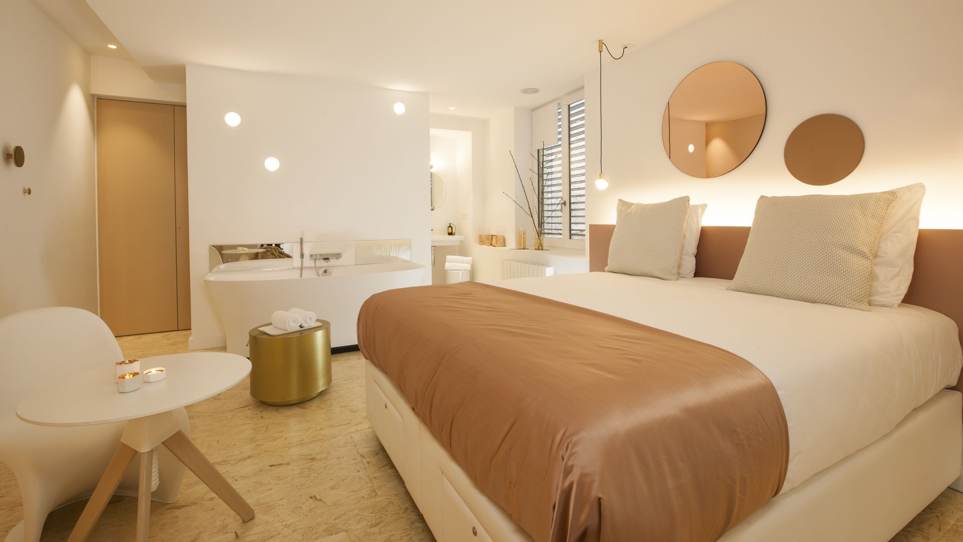 Chambre d'hôtel avec salle de bain ouverte, murs gris, lit, chaises et cheminée.