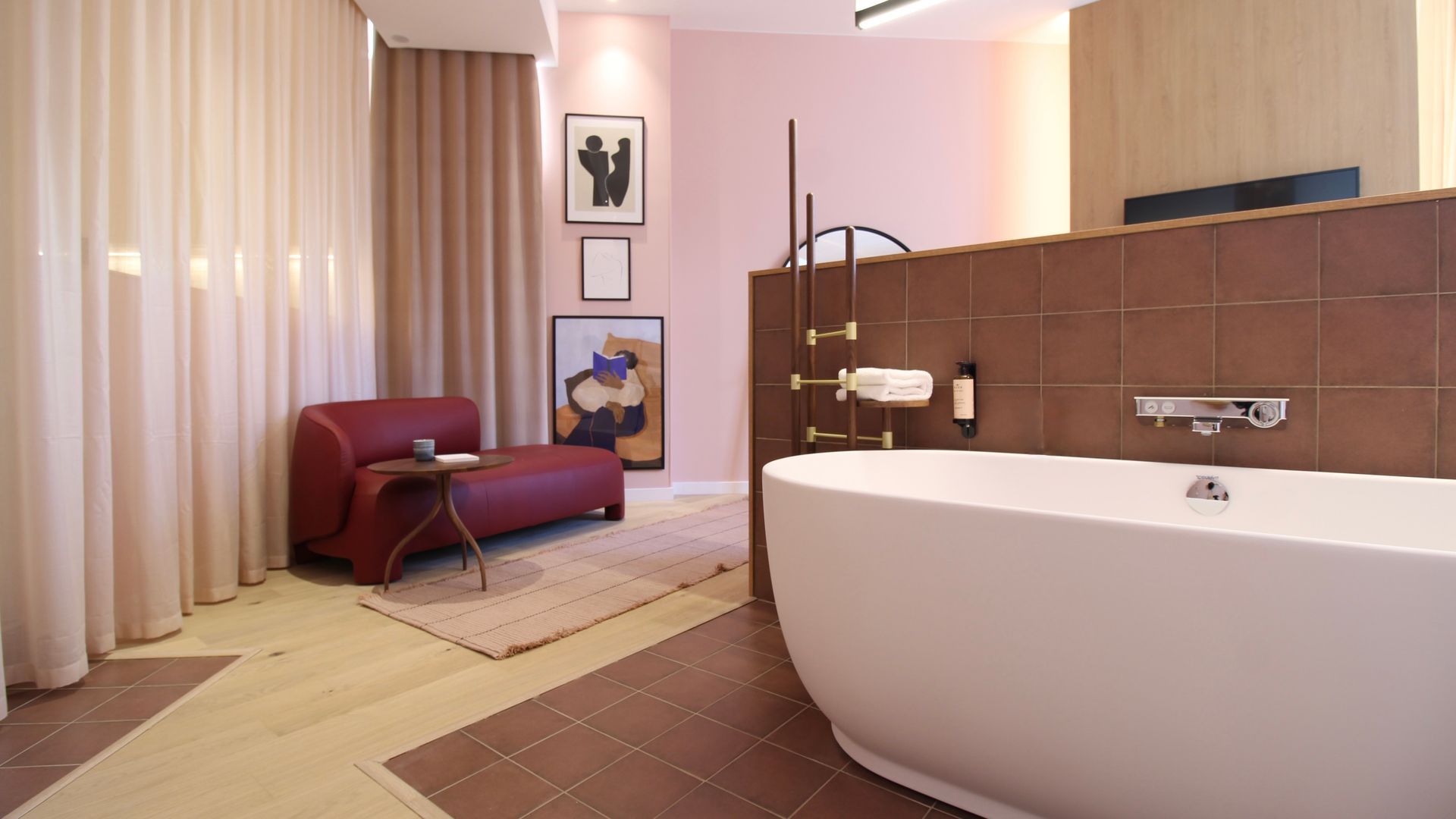 Salle de bains luxueuse avec baignoire îlot, chaise longue rouge et œuvres d'art sur les murs roses.