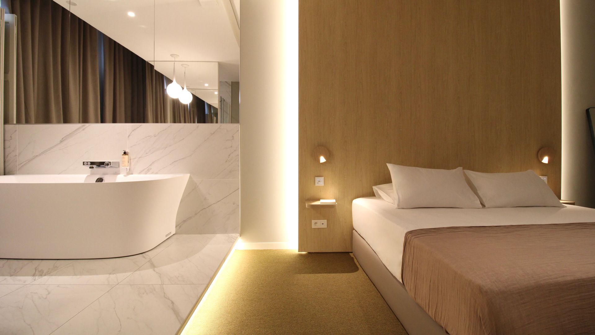 Salle de bains et chambre d'hôtel modernes avec baignoire îlot, sol en marbre et boiseries chaleureuses.