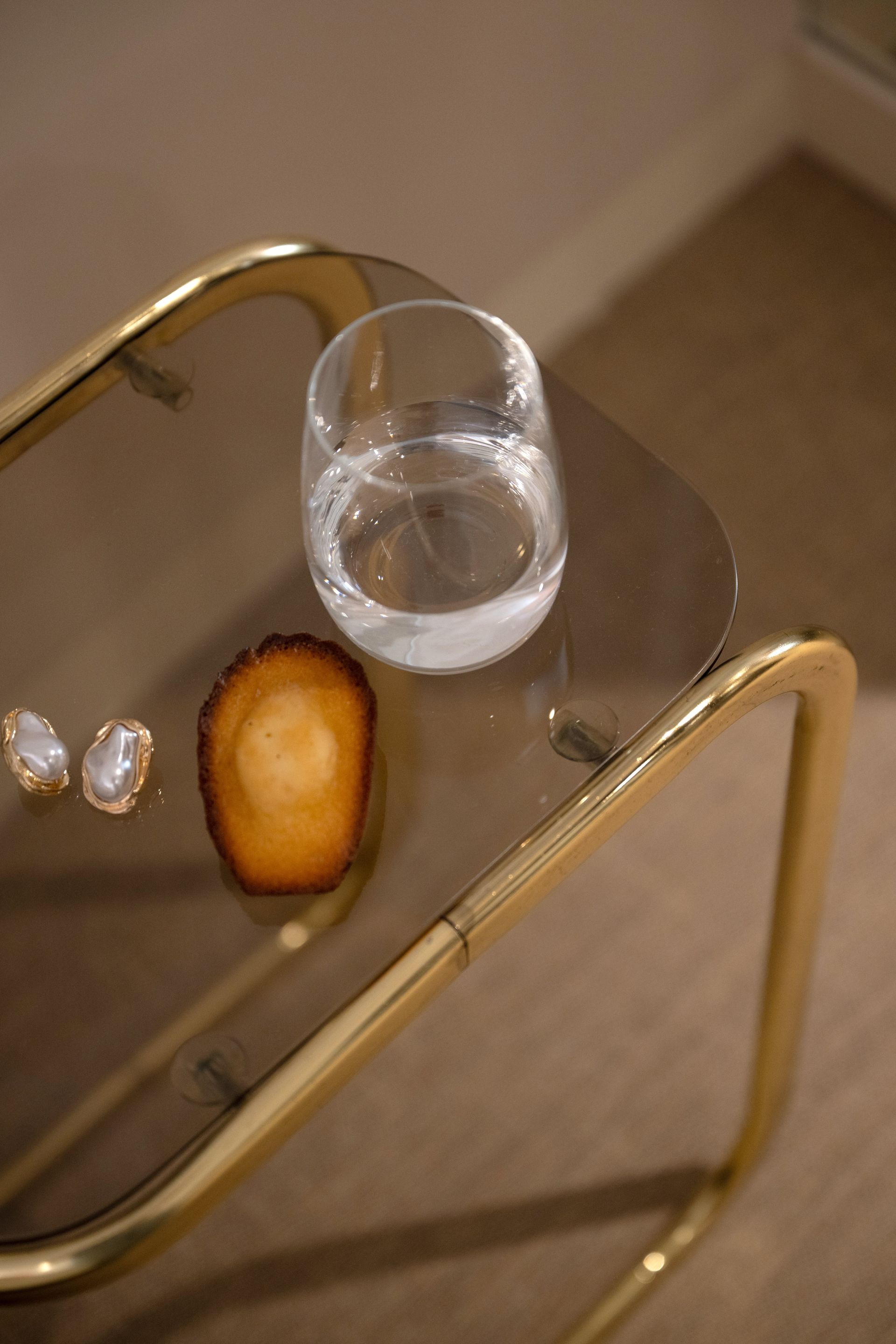 Verre à vin et pâtisserie sur une table d'appoint en laiton à plateau de verre dans une pièce beige