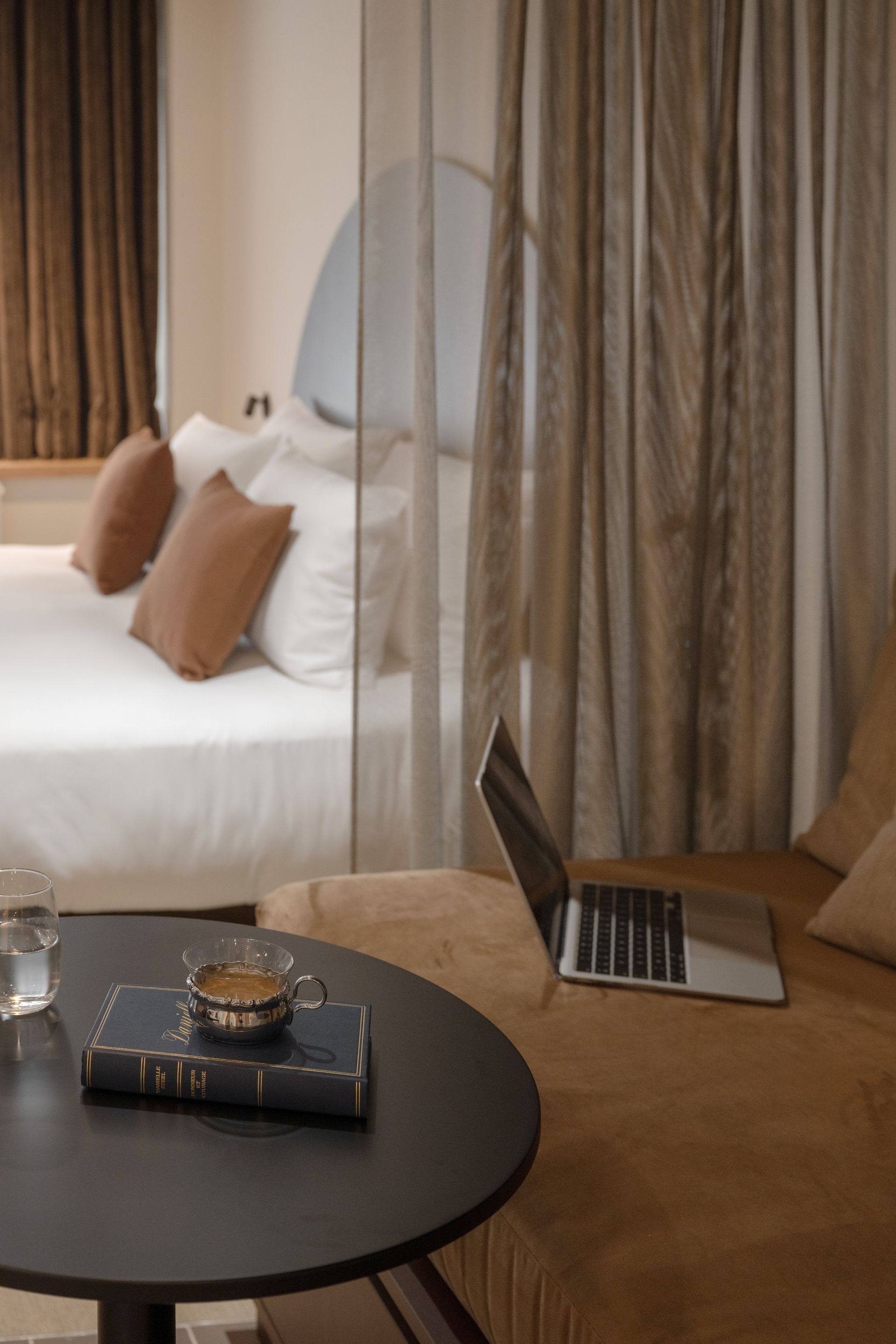 Chambre confortable avec un lit, des rideaux, une table ronde noire et un ordinateur portable sur une chaise près de la fenêtre.
