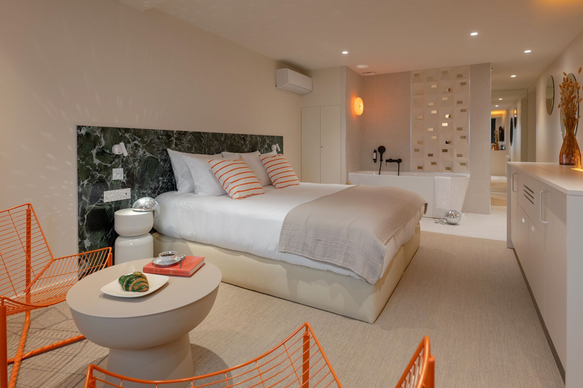 Salle de bains moderne avec baignoire, miroir rond et deux douches ; carrelage beige.
