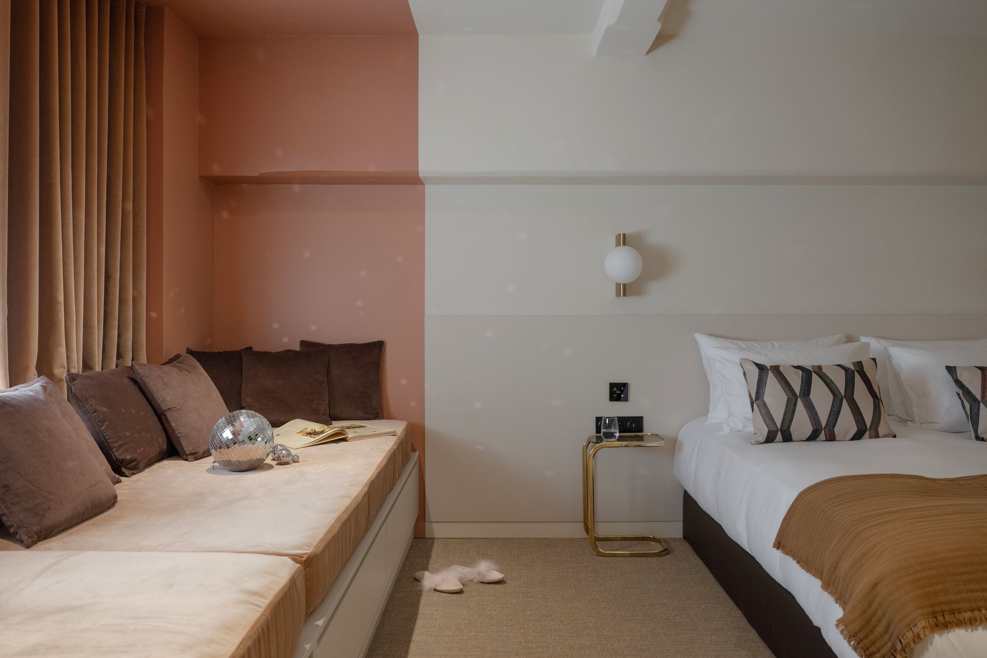 Chambre moderne avec un lit, une banquette près de la fenêtre, une décoration neutre et une petite table de chevet
