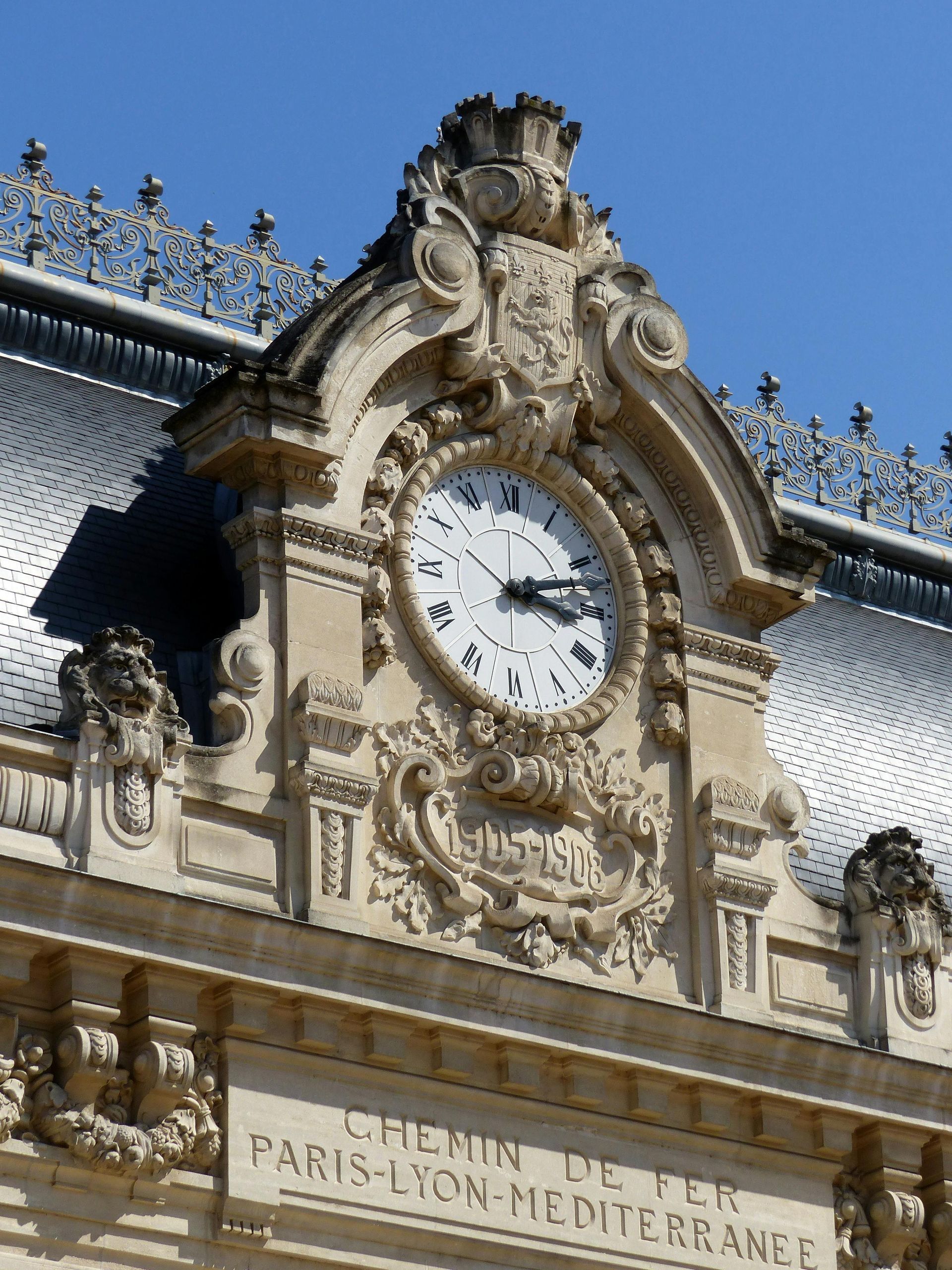 Horloge sur la façade de la gare de Paris-Lyon-Méditerranée, sculptures en pierre ornementées, fond de ciel bleu.