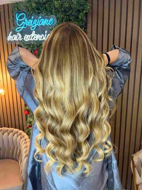 Vista trasera de cabello largo y ondulado, rubio con raíces oscuras, en un salón de belleza