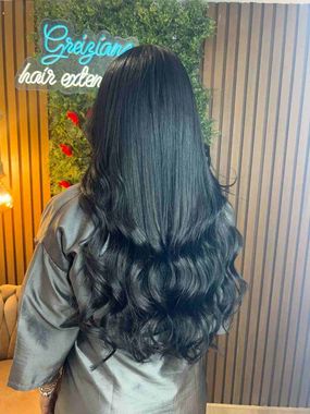 Mujer de pelo negro largo y chaqueta gris, de pie frente a un letrero de neón y una pared revestida de madera
