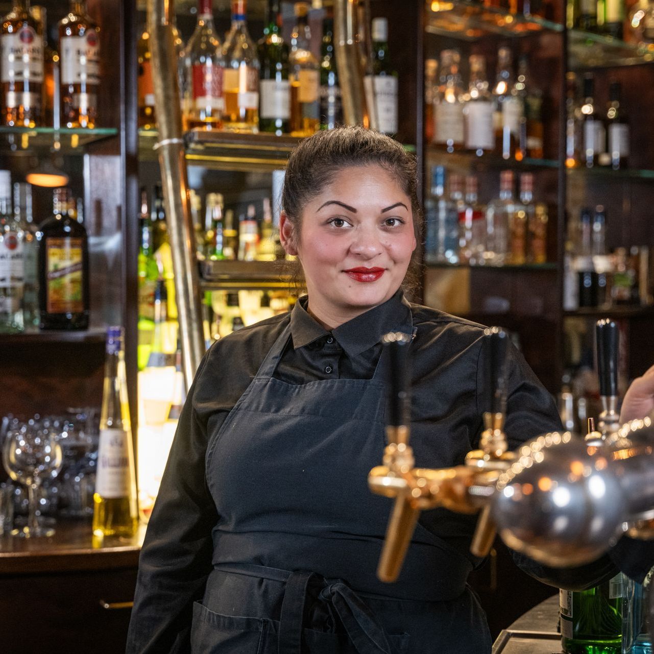 Eine Frau in einer schwarzen Schürze steht an einer Bar.