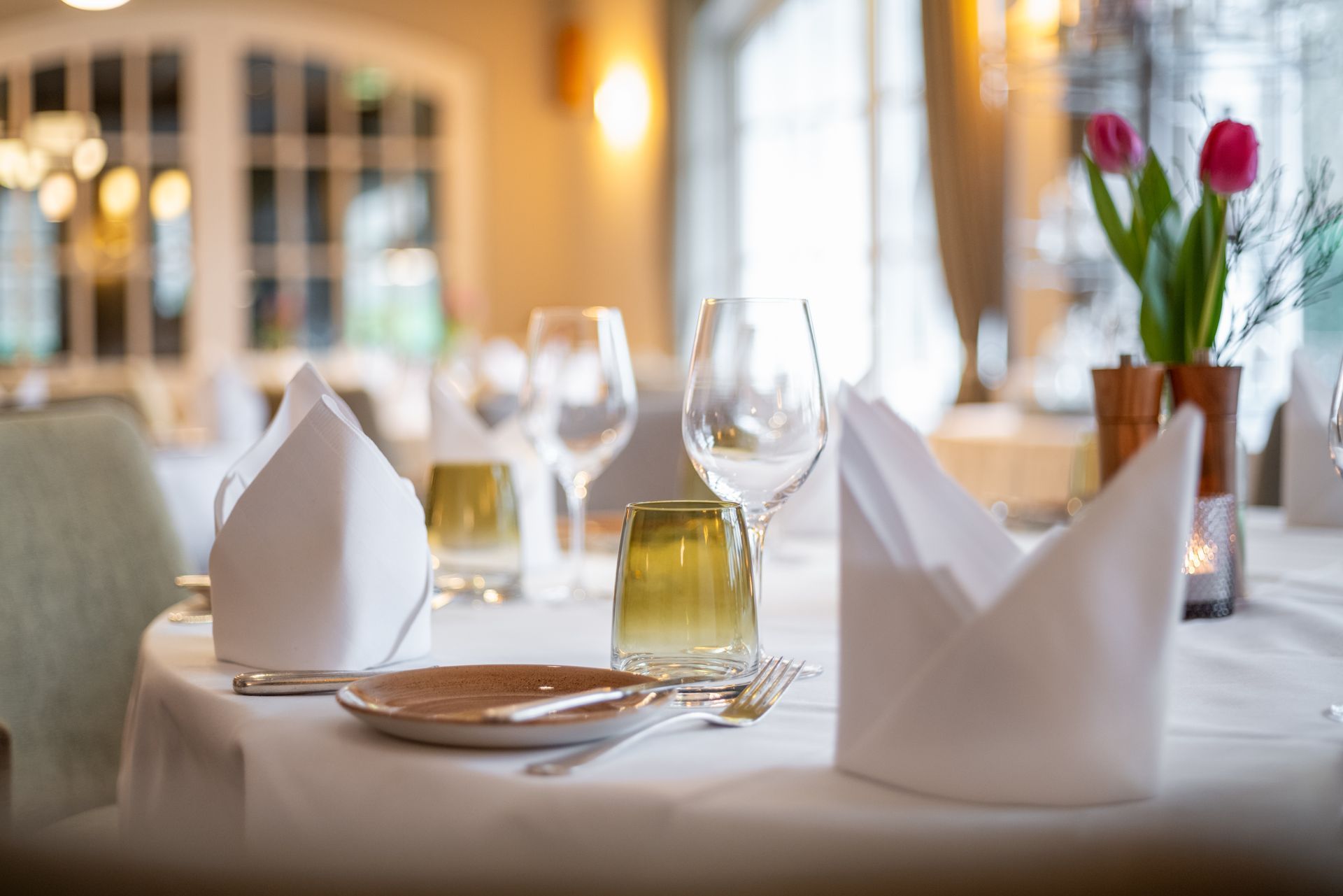 Ein Tisch in einem Restaurant mit Tellern, Gläsern, Servietten und Blumen darauf.