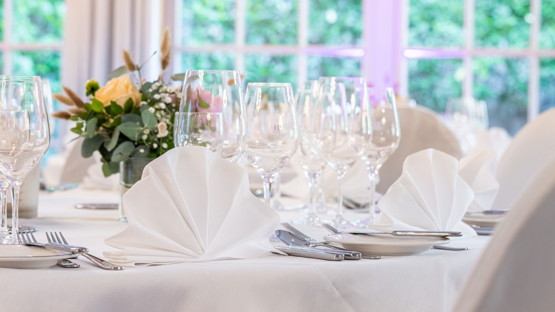 Ein für einen Hochzeitsempfang gedeckter Tisch mit einer Vase mit Blumen darauf.