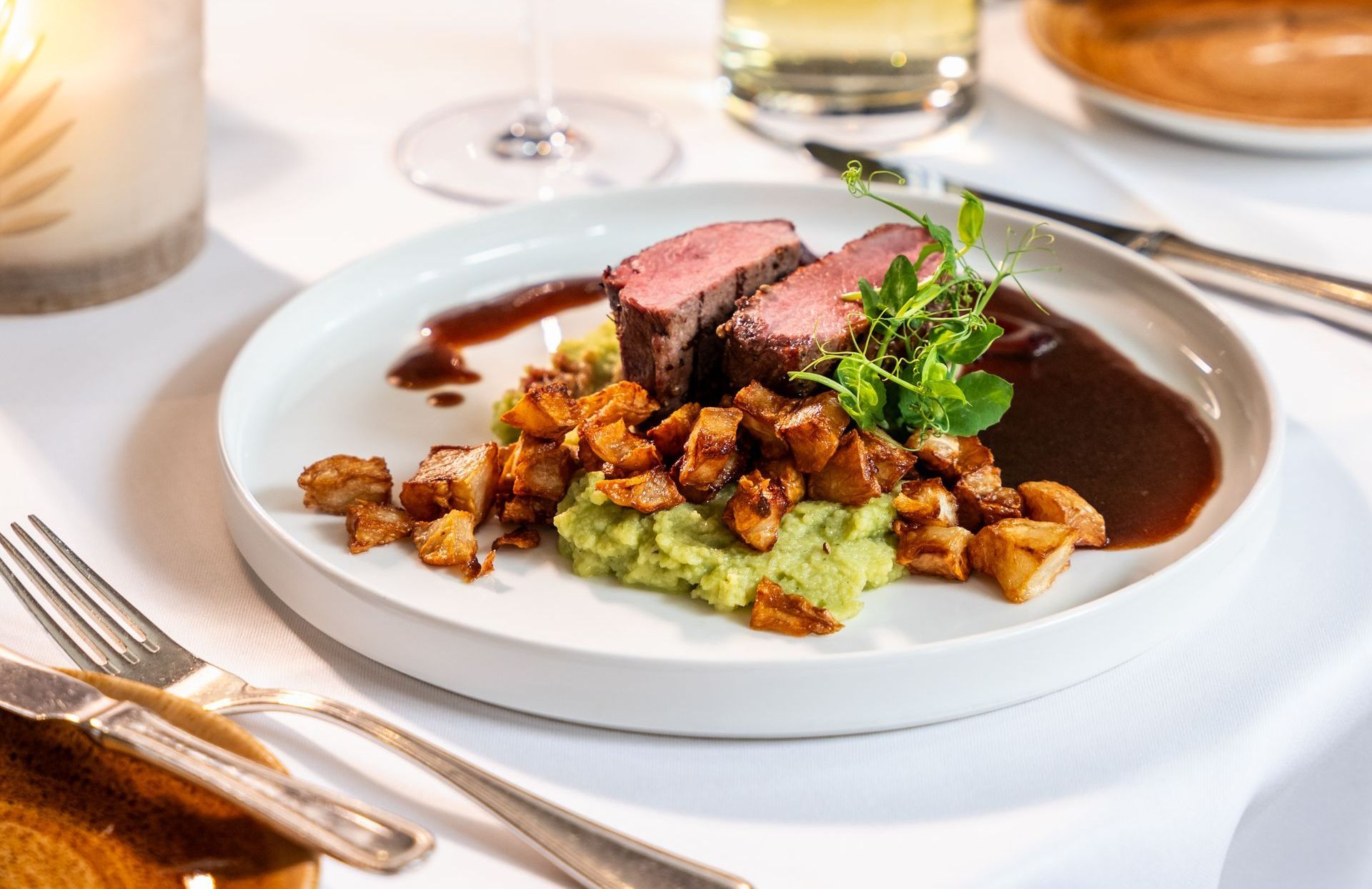 Ein weißer Teller mit Fleisch und Kartoffelbrei auf einem Tisch.