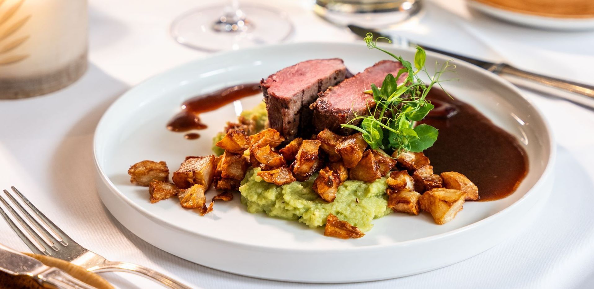 Ein weißer Teller mit Fleisch und Kartoffelbrei auf einem Tisch.