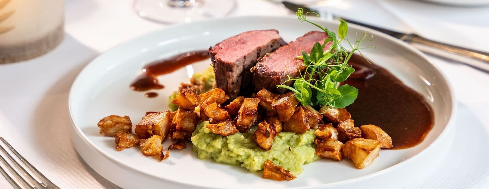 Ein weißer Teller mit Fleisch und Kartoffelbrei auf einem Tisch.