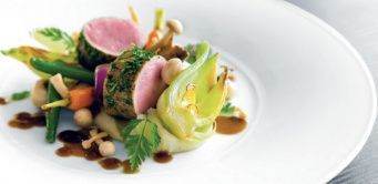 Ein weißer Teller mit Gemüse und Fleisch auf einem Tisch.