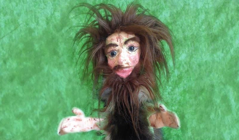 Eine Puppe mit Bart und langen Haaren sitzt auf einer grünen Fläche.