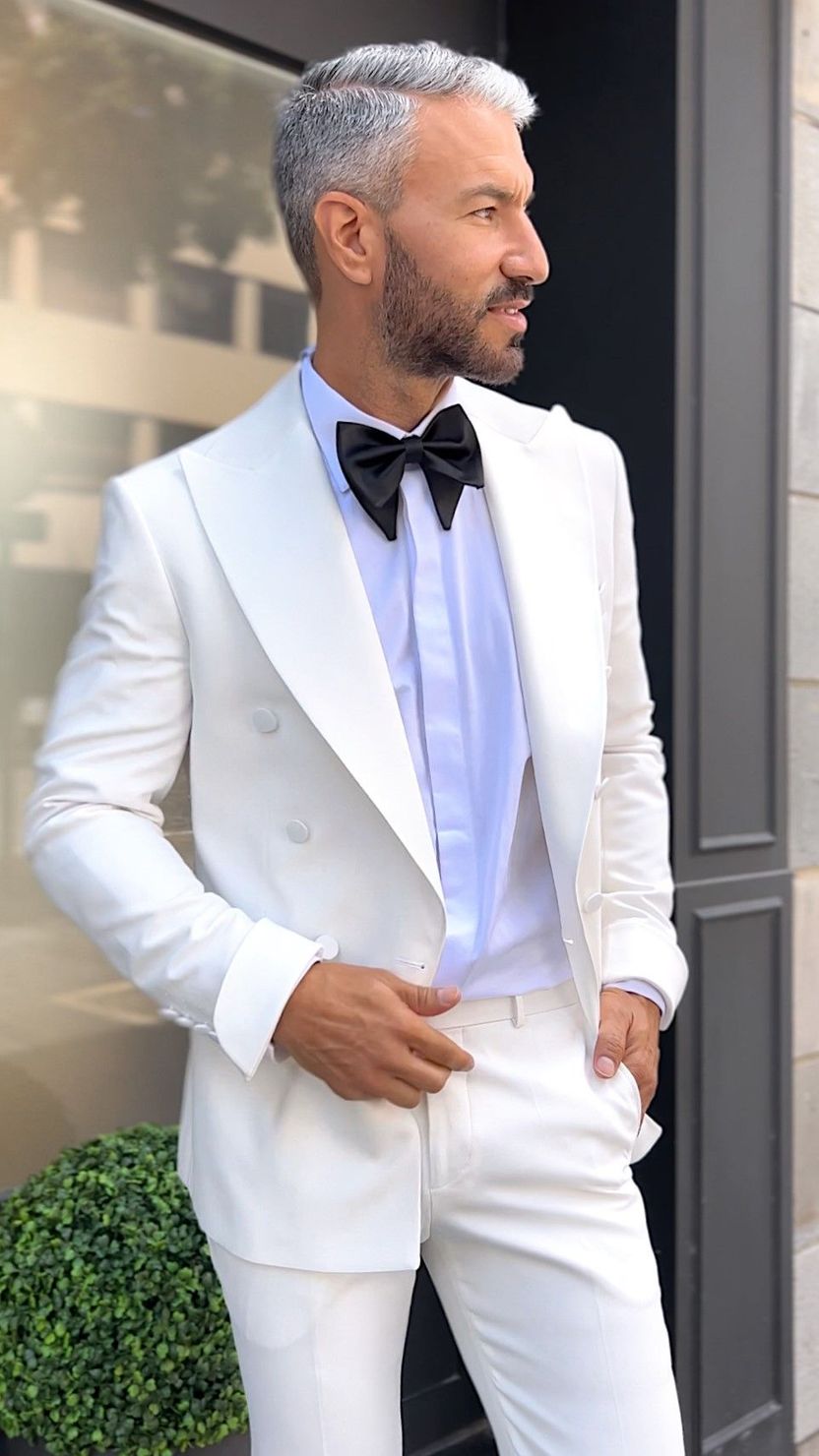 Un hombre con un traje color canela, una pajarita y flores en el bolsillo.
