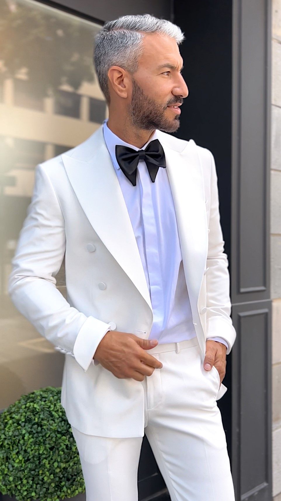 Un hombre con un traje color canela, una pajarita y flores en el bolsillo.