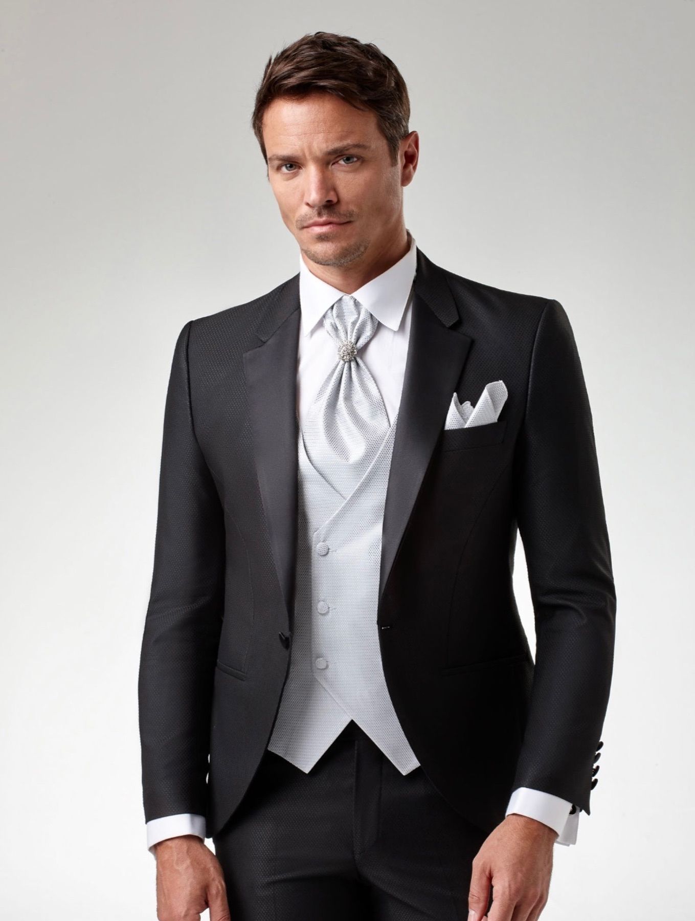 Un hombre lleva un esmoquin negro con chaleco y corbata blancos.