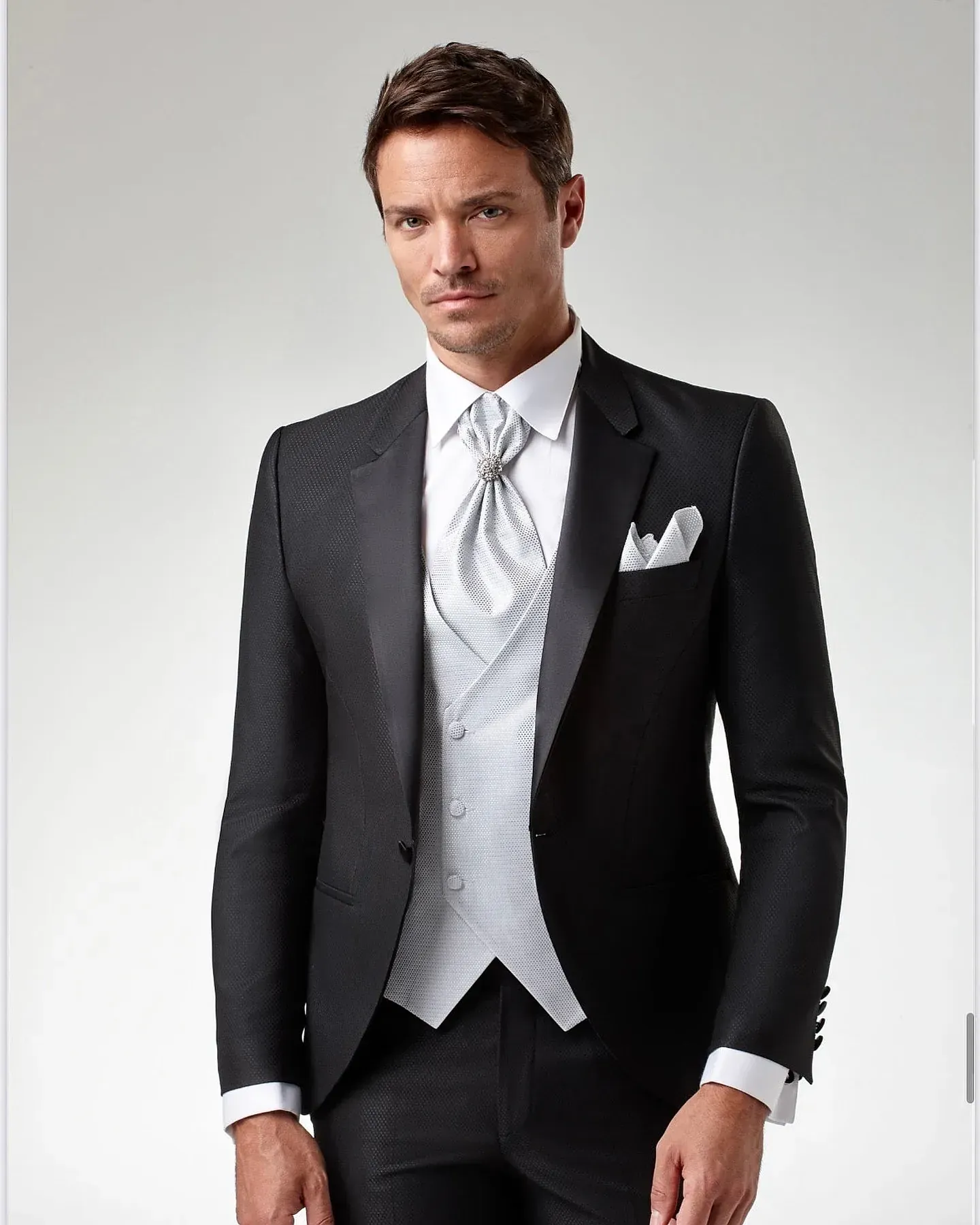 Un hombre con un esmoquin negro, chaleco blanco y corbata.