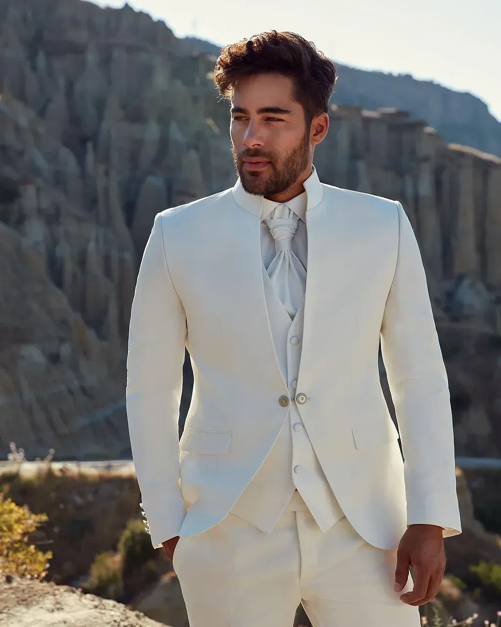 Un hombre con traje blanco y corbata está parado frente a una montaña.