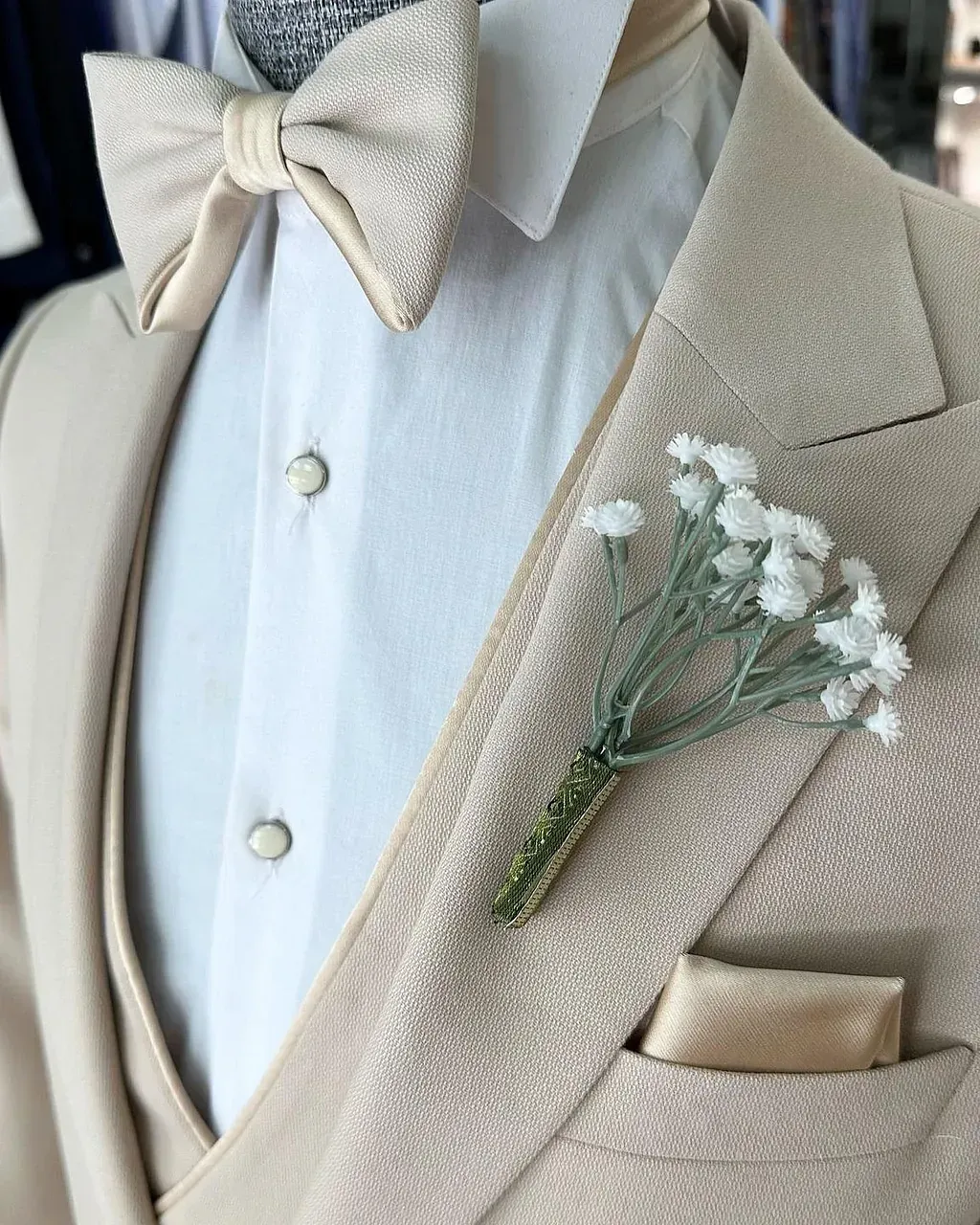 Un hombre con un traje color canela, una pajarita y flores en el bolsillo.